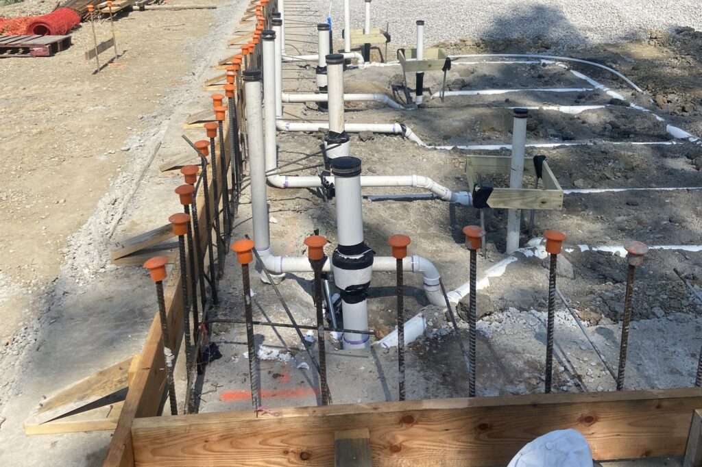 Under-slab plumbing rough-in before the concrete pour: PVC drain stubs and capped rebar inside the forms
