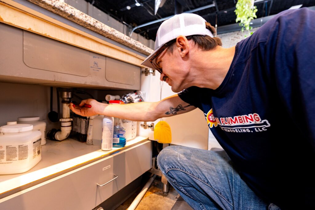 Tulsa Plumbing & Remodeling technician reaching in to the drain trap under a sink