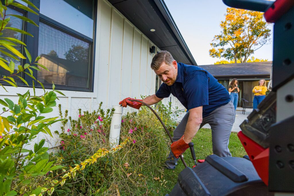Tulsa Plumbing & Remodeling technician running a drain cleaning machine into a cleanout beside a house