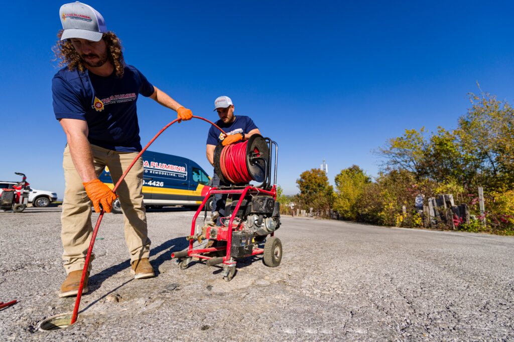 Two Tulsa Plumbing & Remodeling technicians feeding a hydro jetter hose into a cleanout
