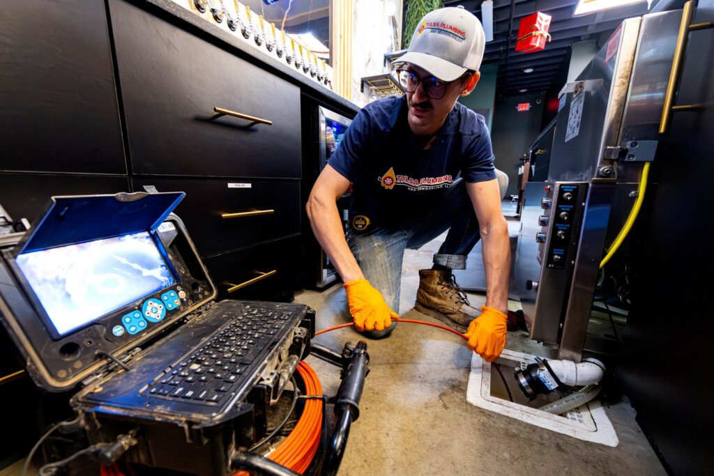 Tulsa Plumbing & Remodeling technician running a sewer camera down a floor drain, with the camera screen open