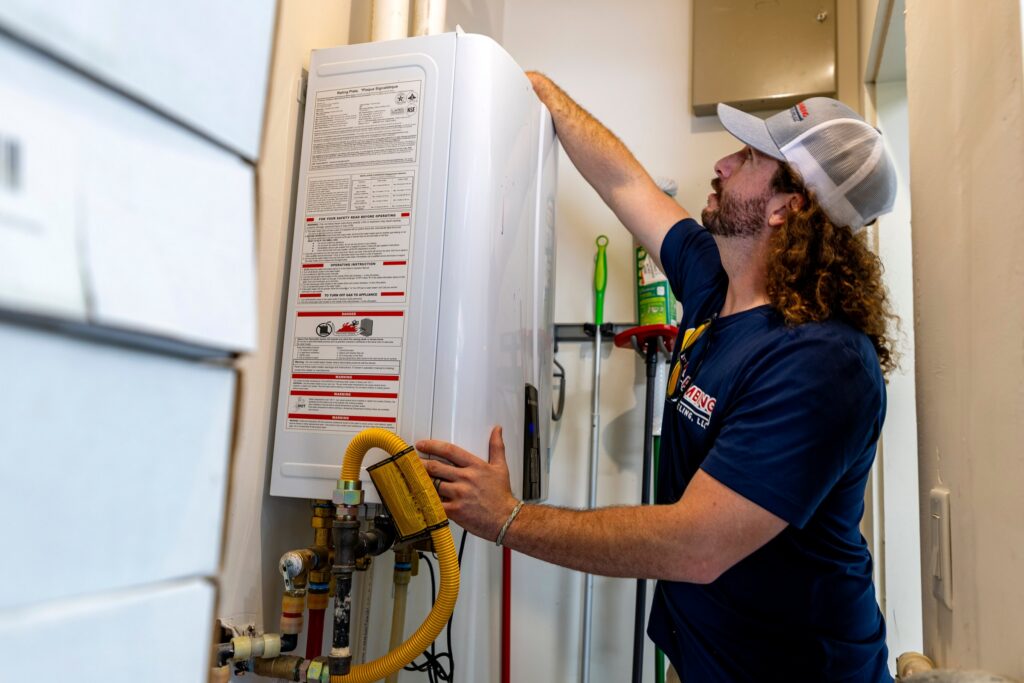 A Tulsa Plumbing & Remodeling technician checking a wall-mounted tankless water heater.